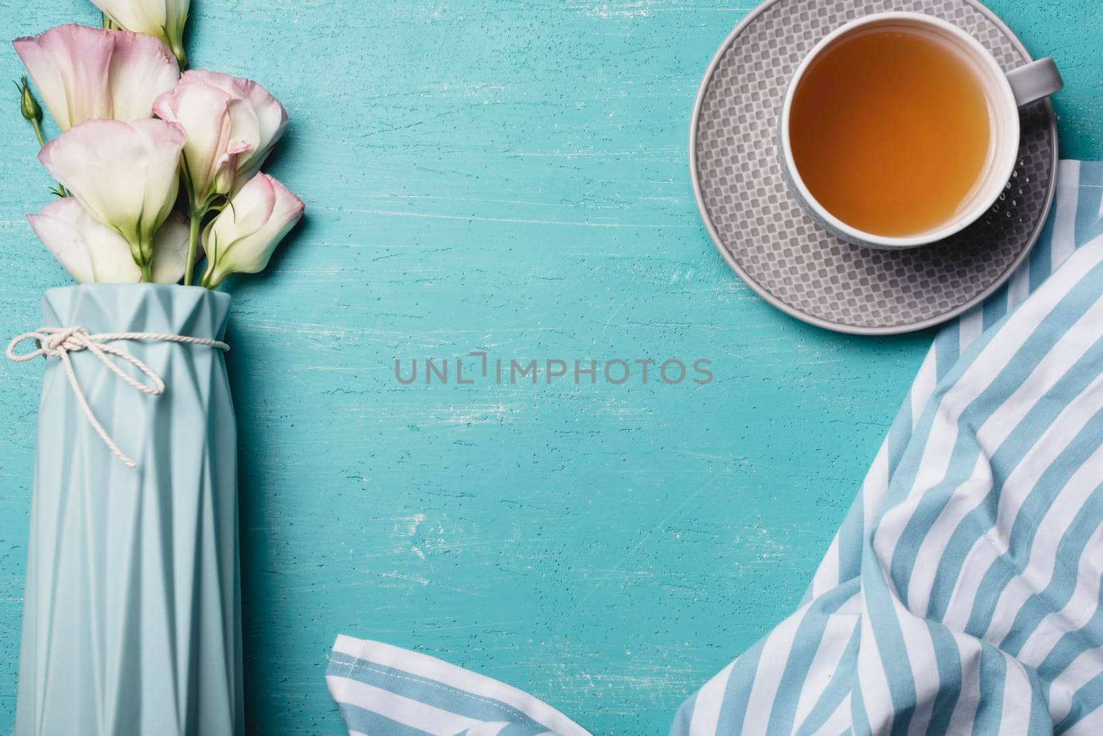 eustoma flower vase with cup tea napkin blue background