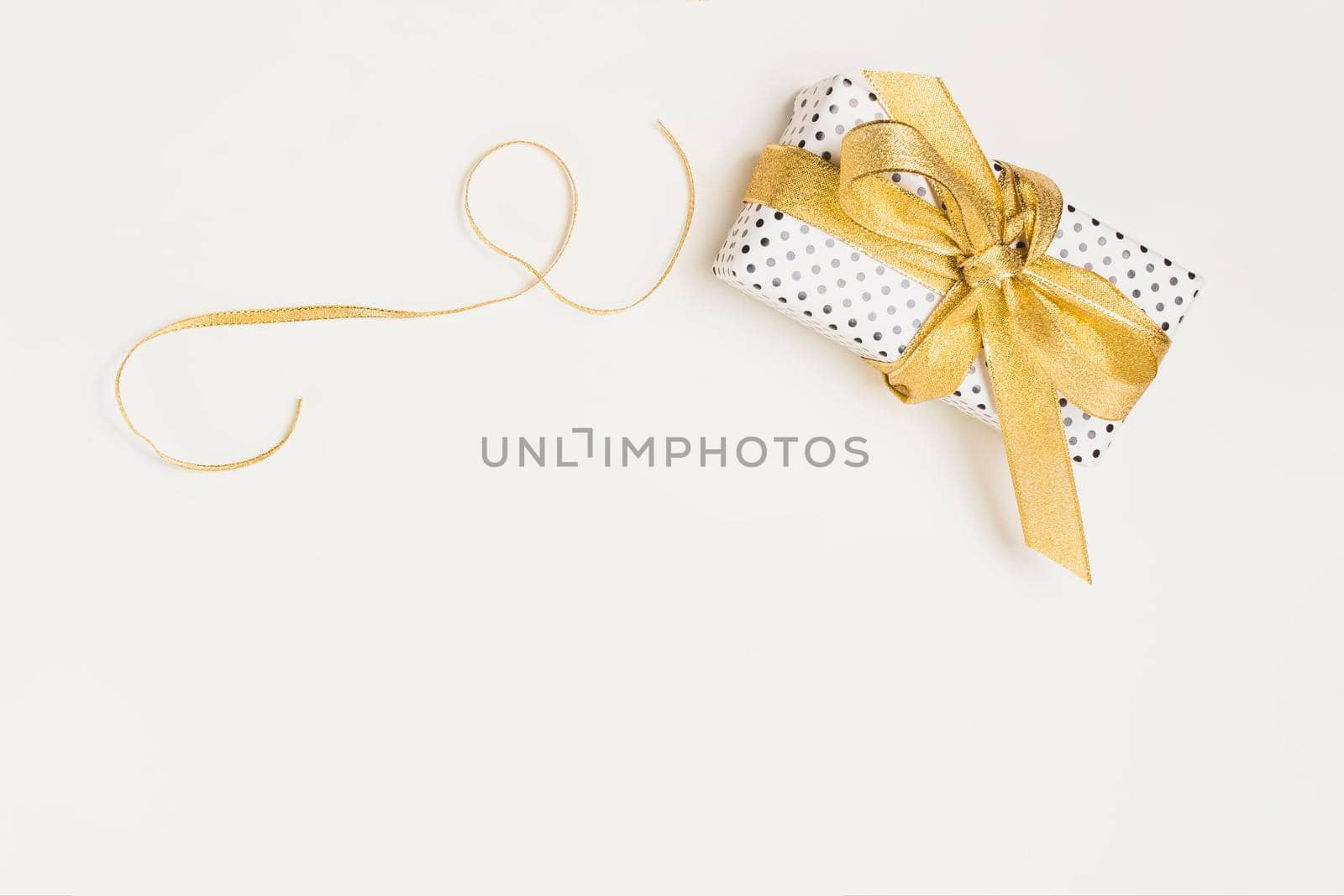 elevated view present box wrapped polka dot design paper with shiny golden ribbon isolated white backdrop by Zahard