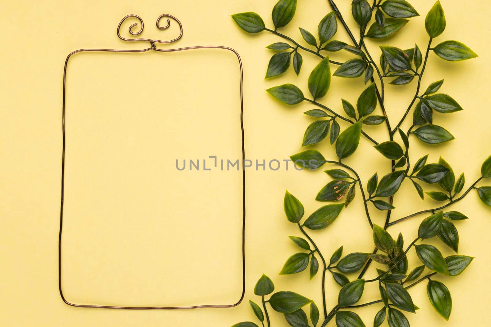 empty metallic frame near artificial leaves yellow wall