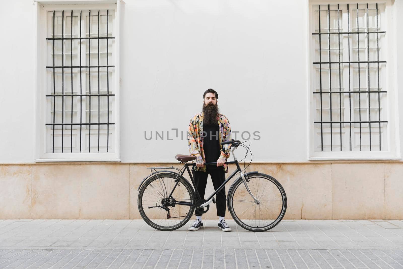 bearded young man standing with bicycle against wall by Zahard