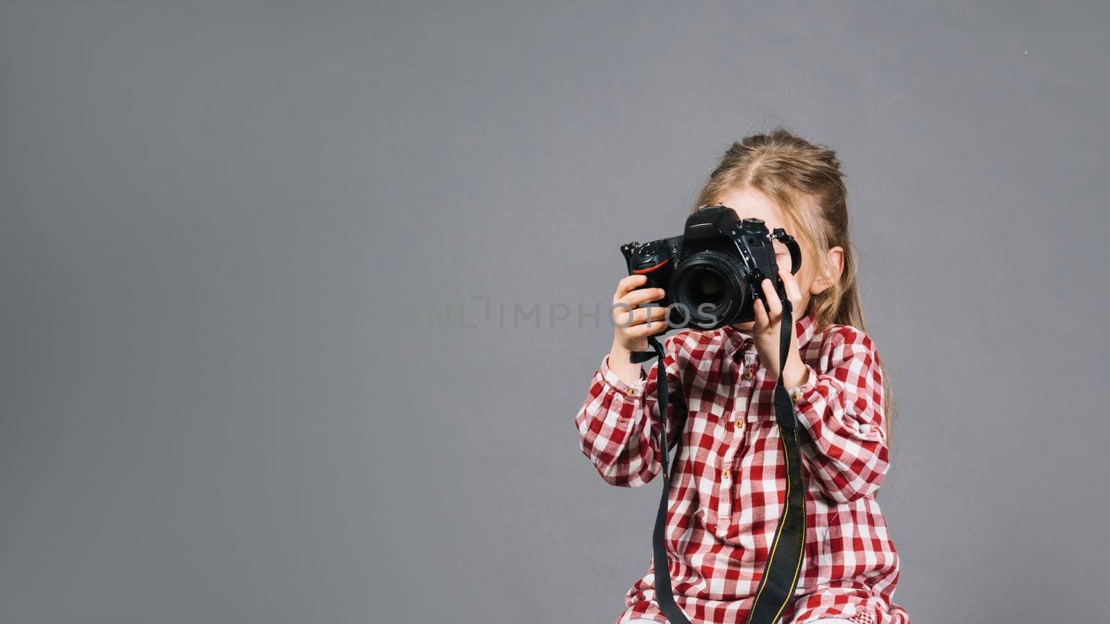 close up girl holding camera front her face standing against gray backdrop