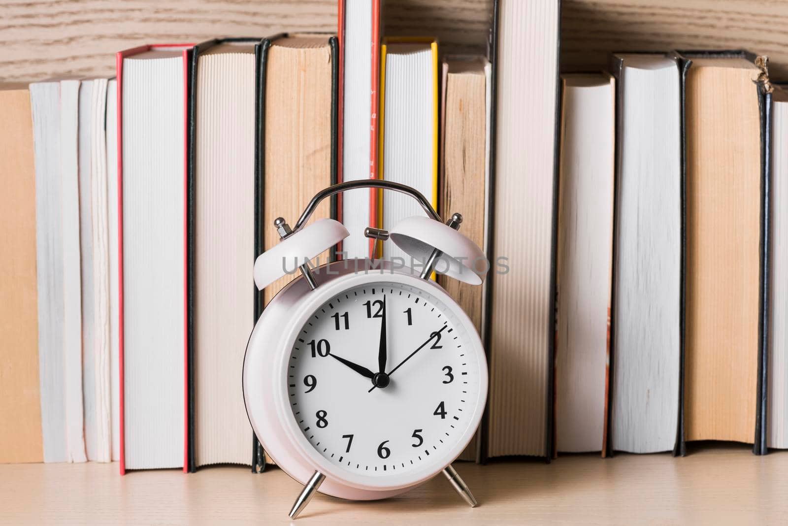 white alarm clock showing 10 o clock front bookshelf wooden desk
