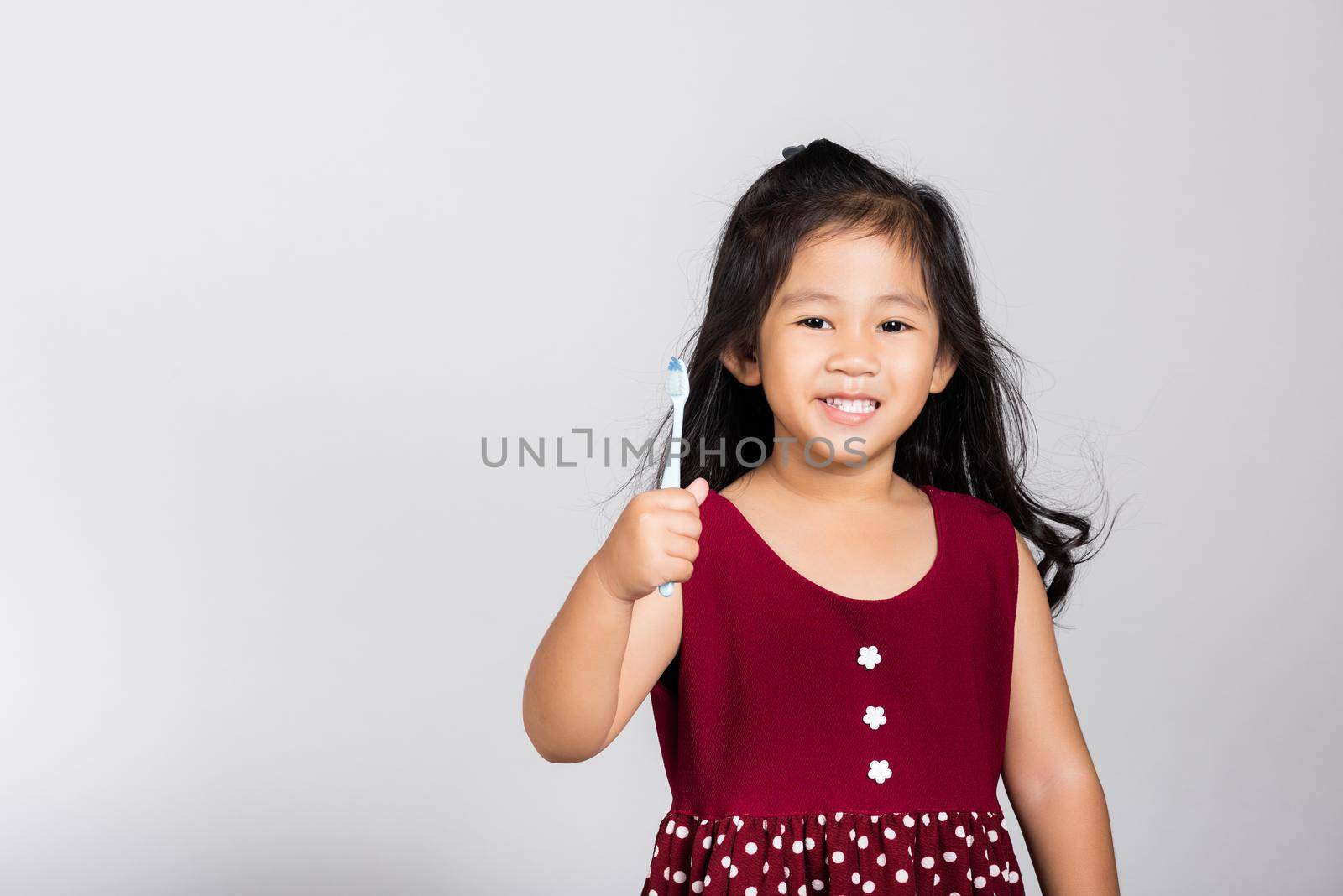 Little cute kid girl 3-4 years old show brush teeth and smile in studio shot isolated on white background, happy Asian children holding toothbrush in mouth by himself, Dental hygiene healthy concept
