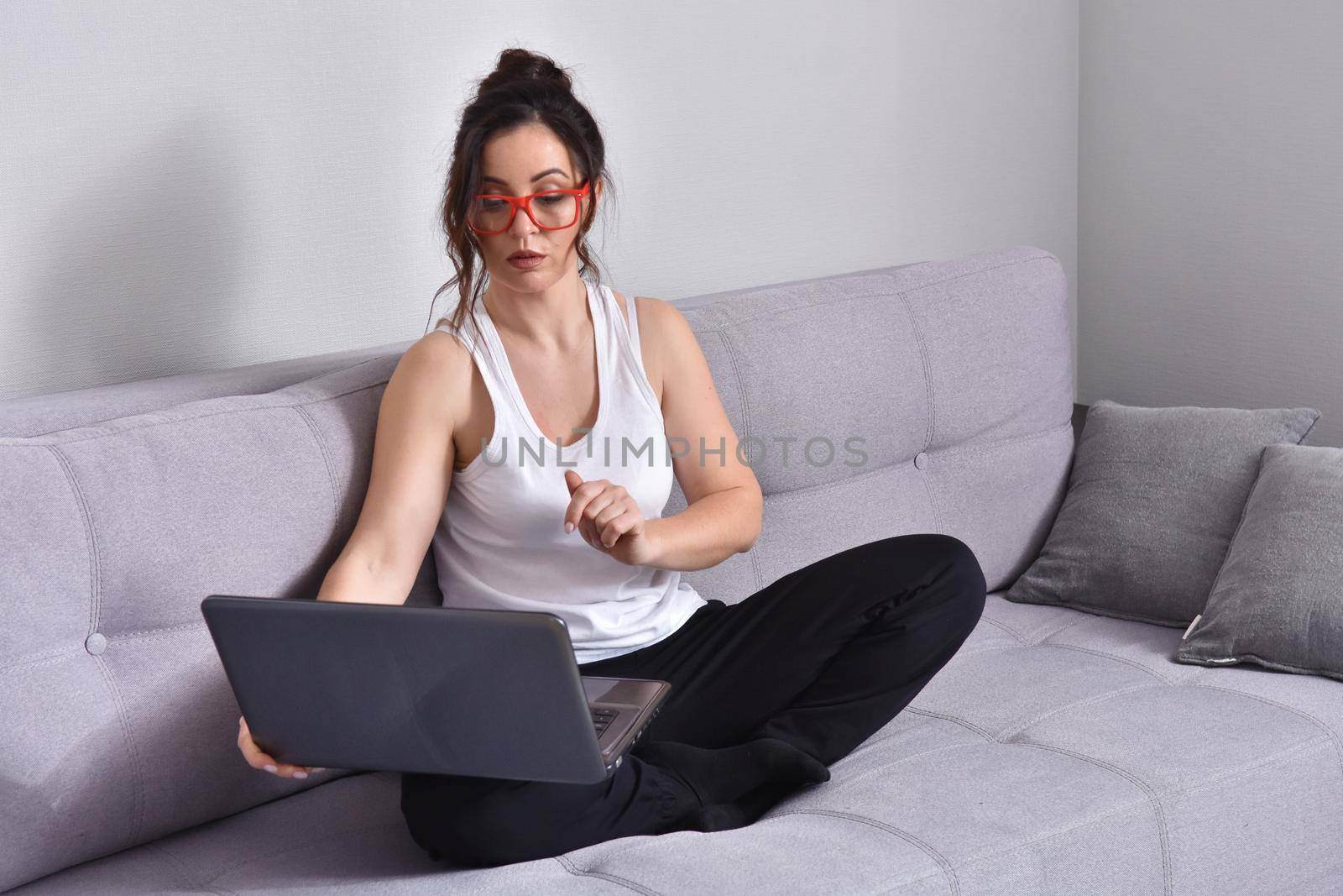 Beautiful brunette woman in red glasses on sofa using laptop