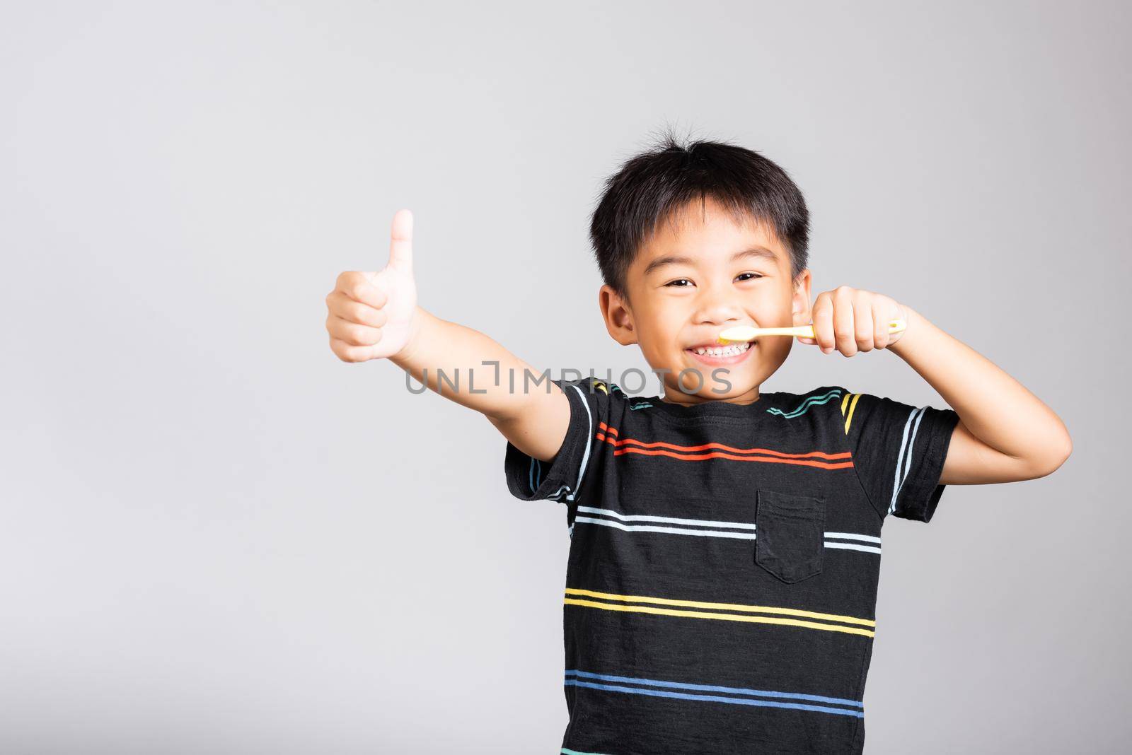 Little cute kid boy 5-6 years old smile brushing teeth and show thumb up finger for good sign in studio shot isolated on white background, happy Asian children, Dental hygiene healthy concept