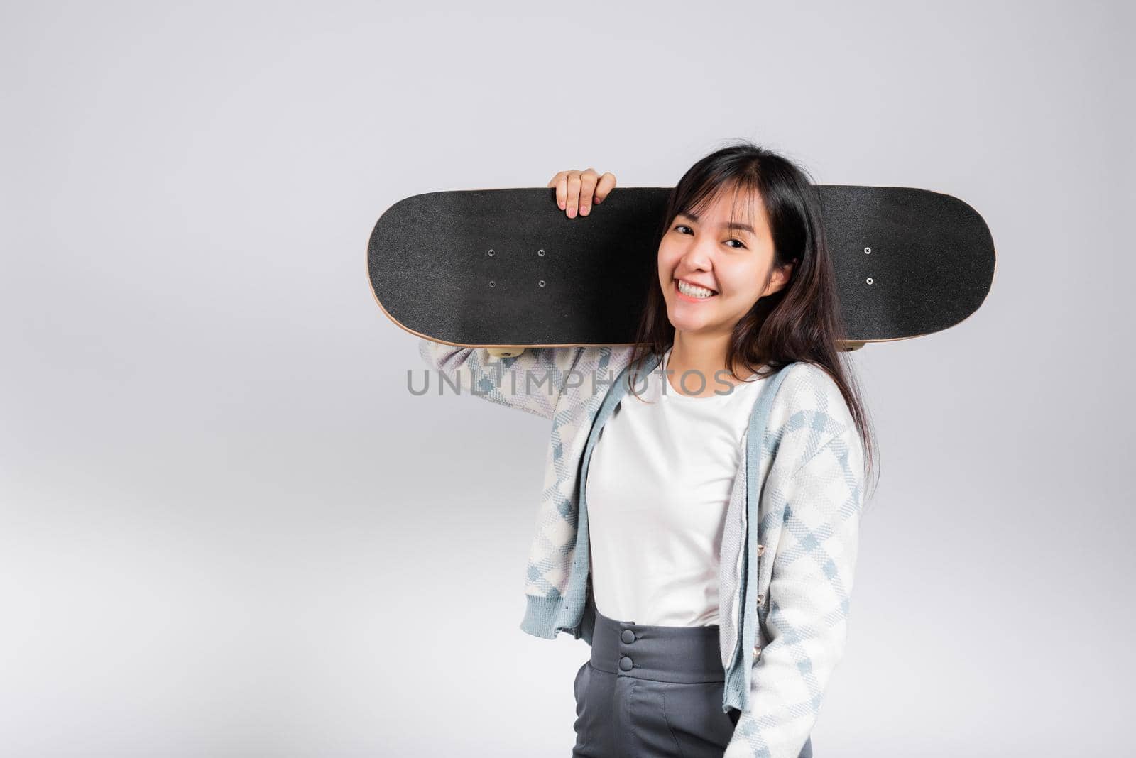 Smiling happy woman holding skateboard on shoulder, Happy Asian beautiful young female excited hold hands longboard, studio shot isolated on white background with copy space, sport extreme