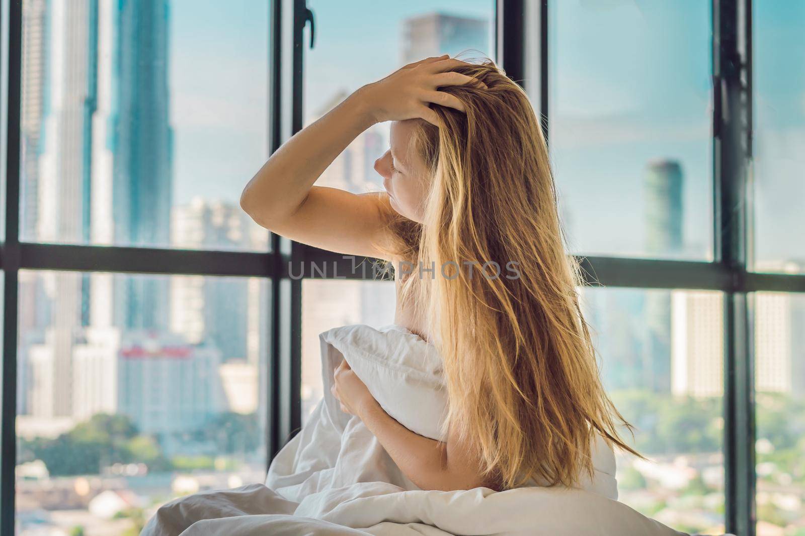 Woman wakes up in the morning in an apartment in the downtown area with a view of the skyscrapers. Life in the noise of the big city concept. Not enough sleep.