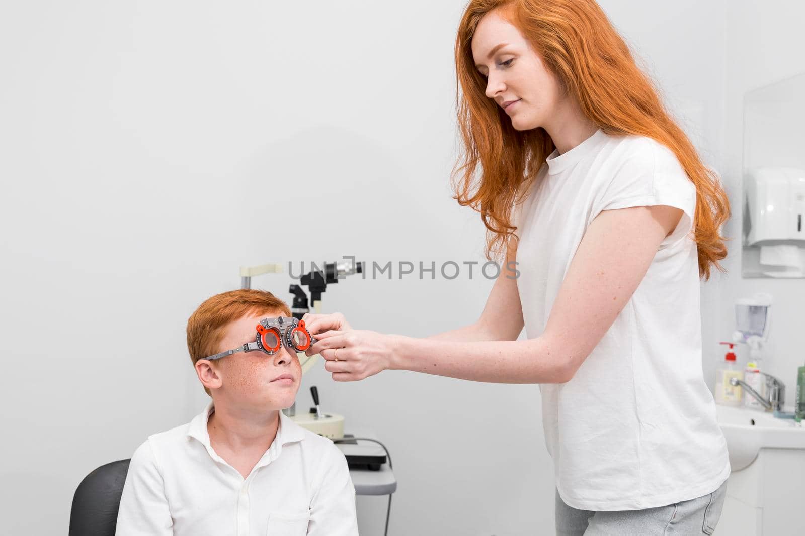 female ophthalmologist examining boy eyes with optometrist trial frame by Zahard