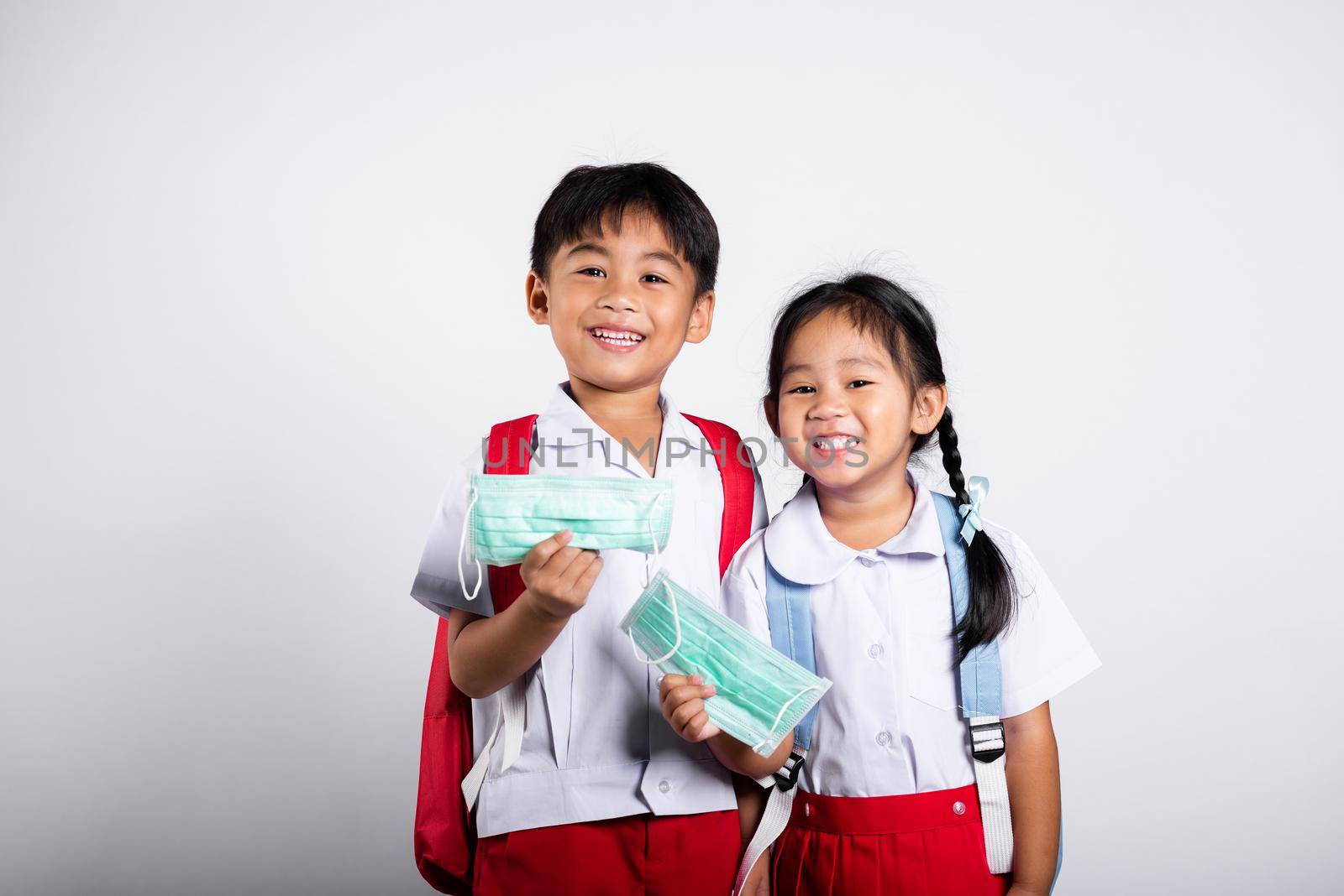 Two Asian student kid girl boy brother sister wearing student thai uniform holding protect mask ready to go to school in studio shot isolated on white background, new normal back to school