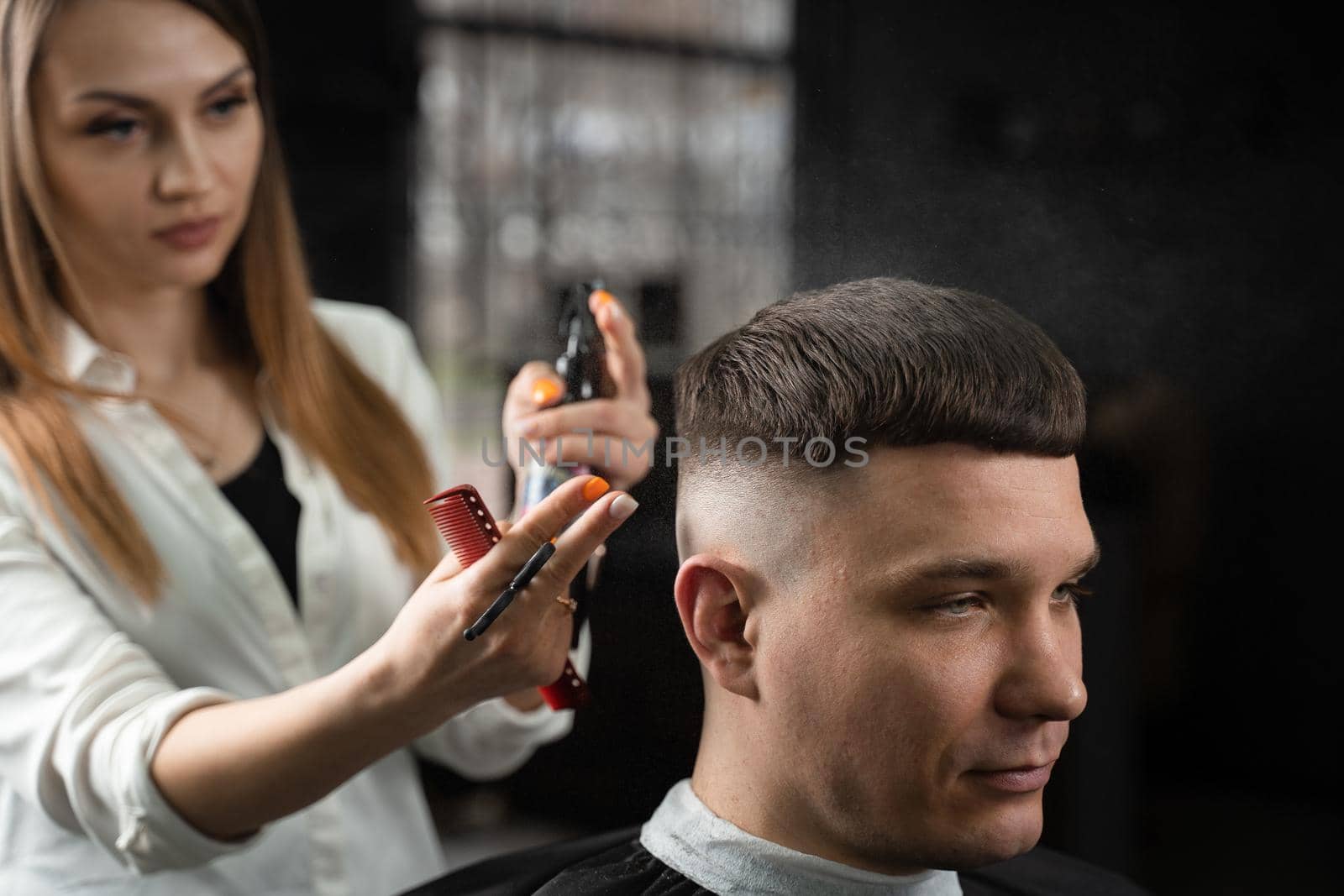 Woman barber making hairstyle in barbershop using clipper. Hairdresser cutting hair of handsome man