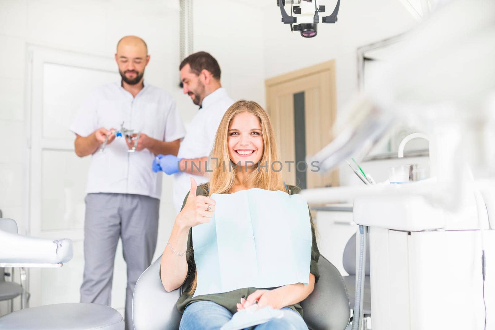 smiling female patient gesturing ok sign front two male dentist by Zahard
