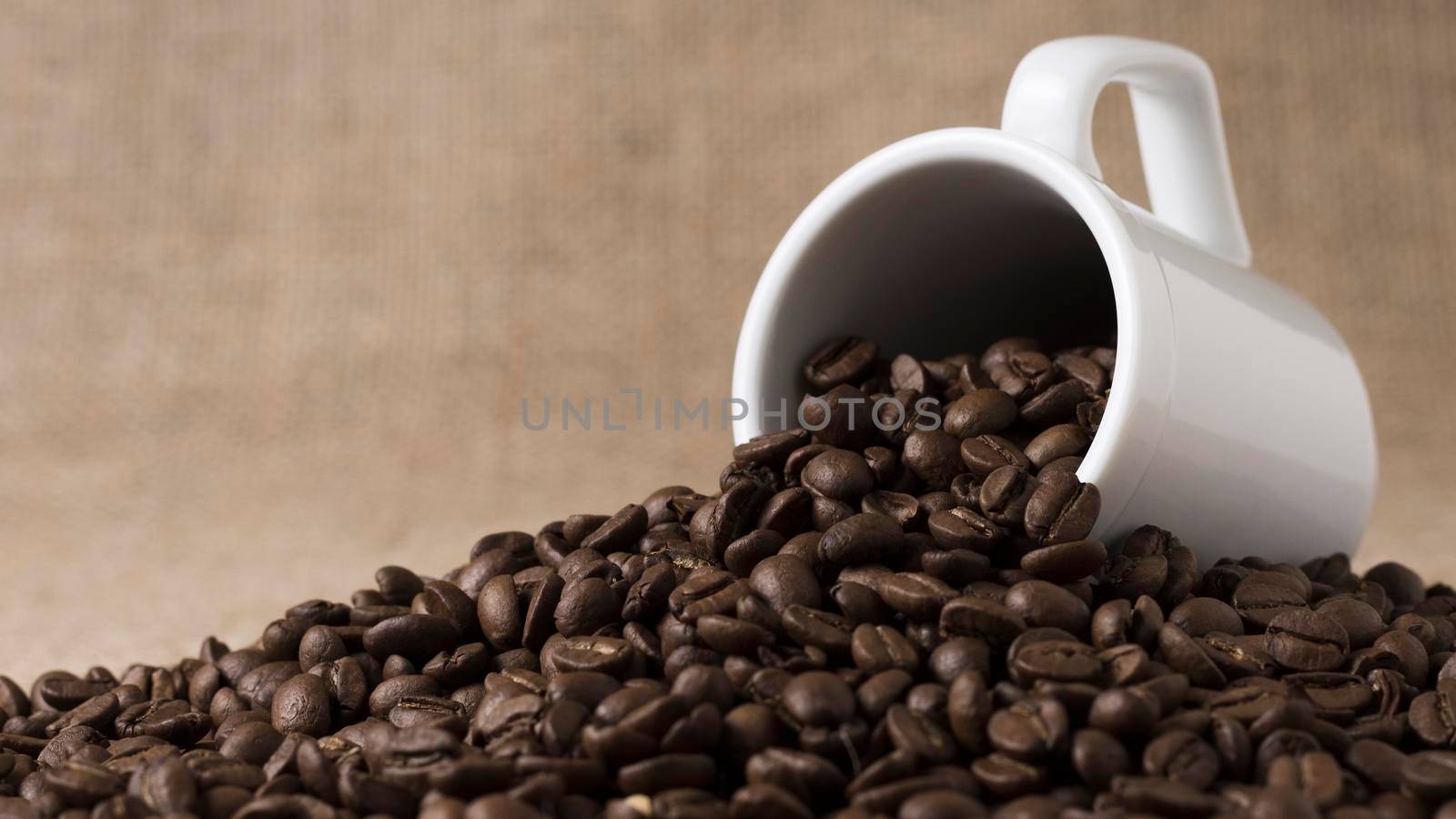 front view roasted coffee beans spilled from white mug