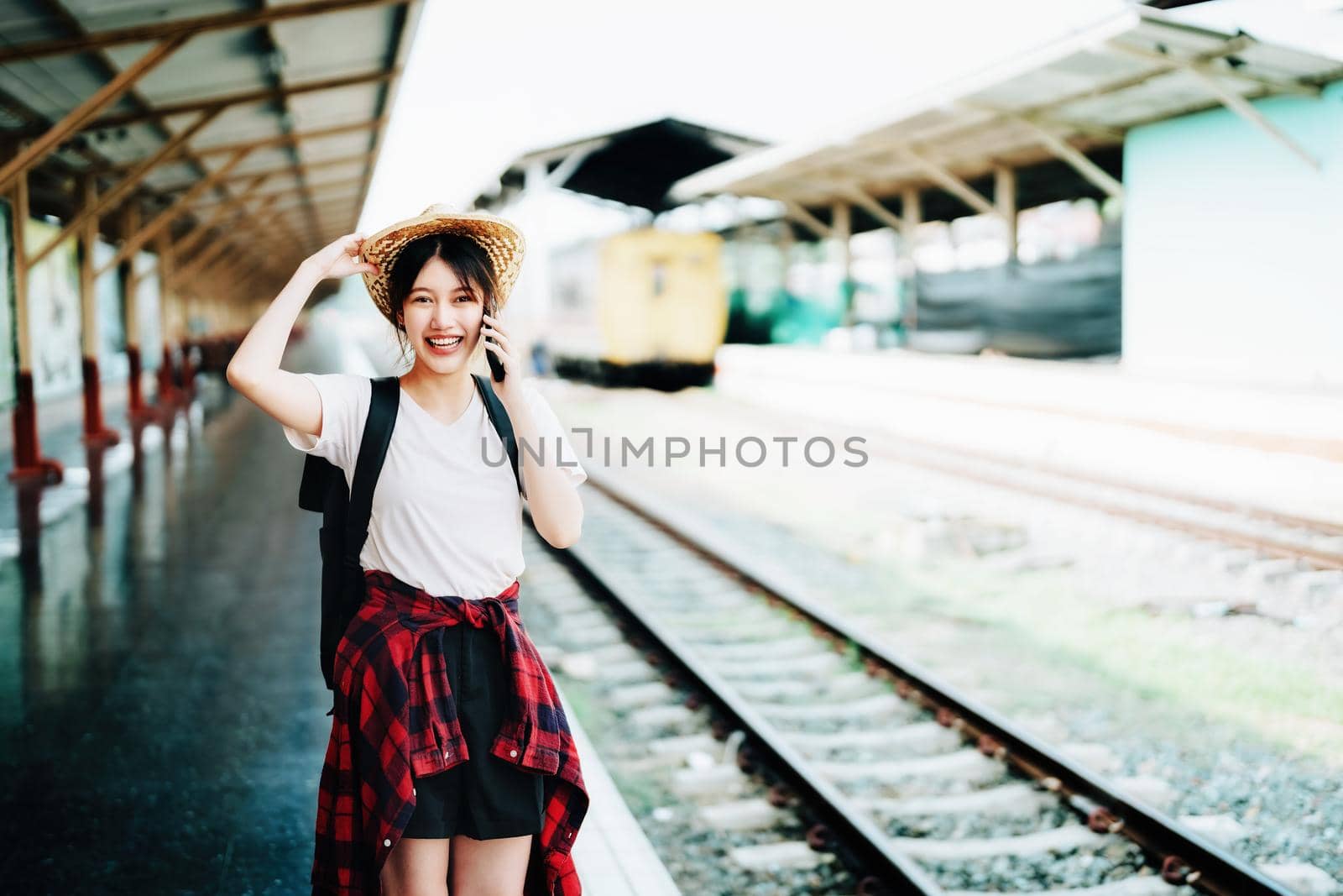 summer, relax, vacation, travel, portrait of beautiful Asian girl using the smartphone mobile to call friends at the train station while waiting for their travel time. by Manastrong