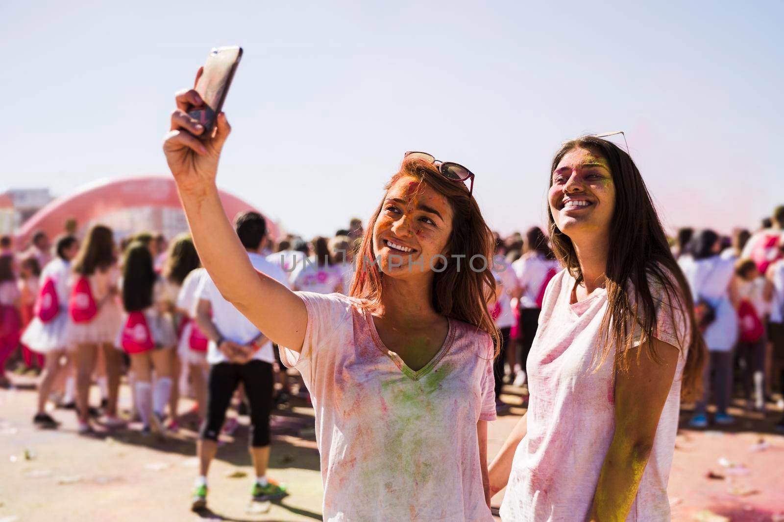 portrait happy young women taking selfie mobile phone during holi festival by Zahard