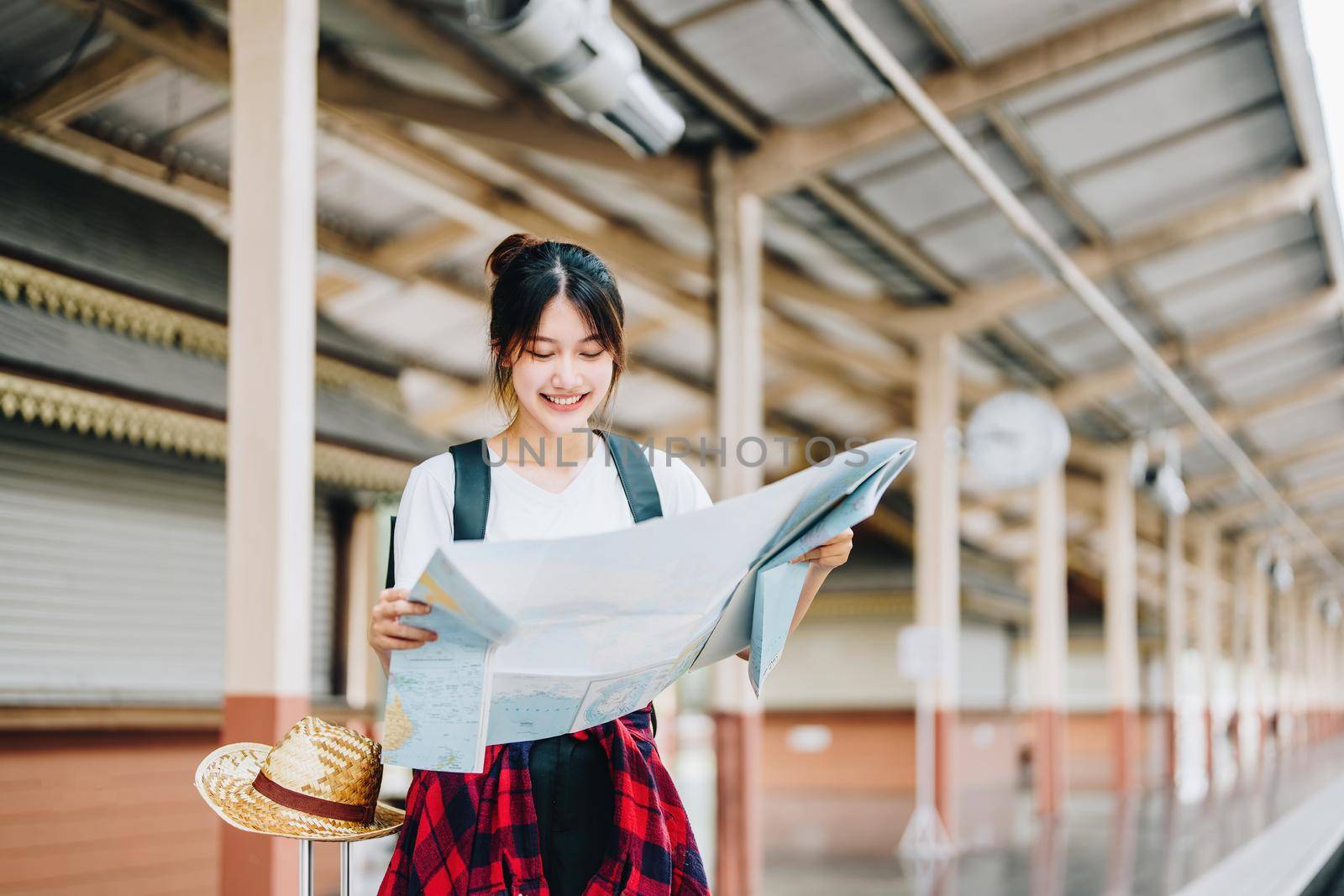 summer, relax, vacation, travel, portrait of a cute Asian girl looking at a map to plan a trip while waiting at the train station