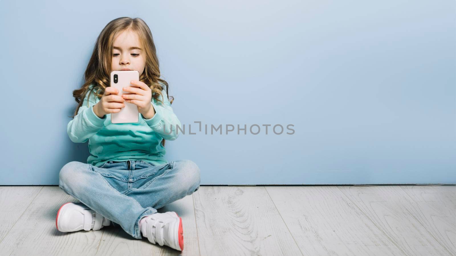 portrait little girl sitting hardwood floor looking smartphone