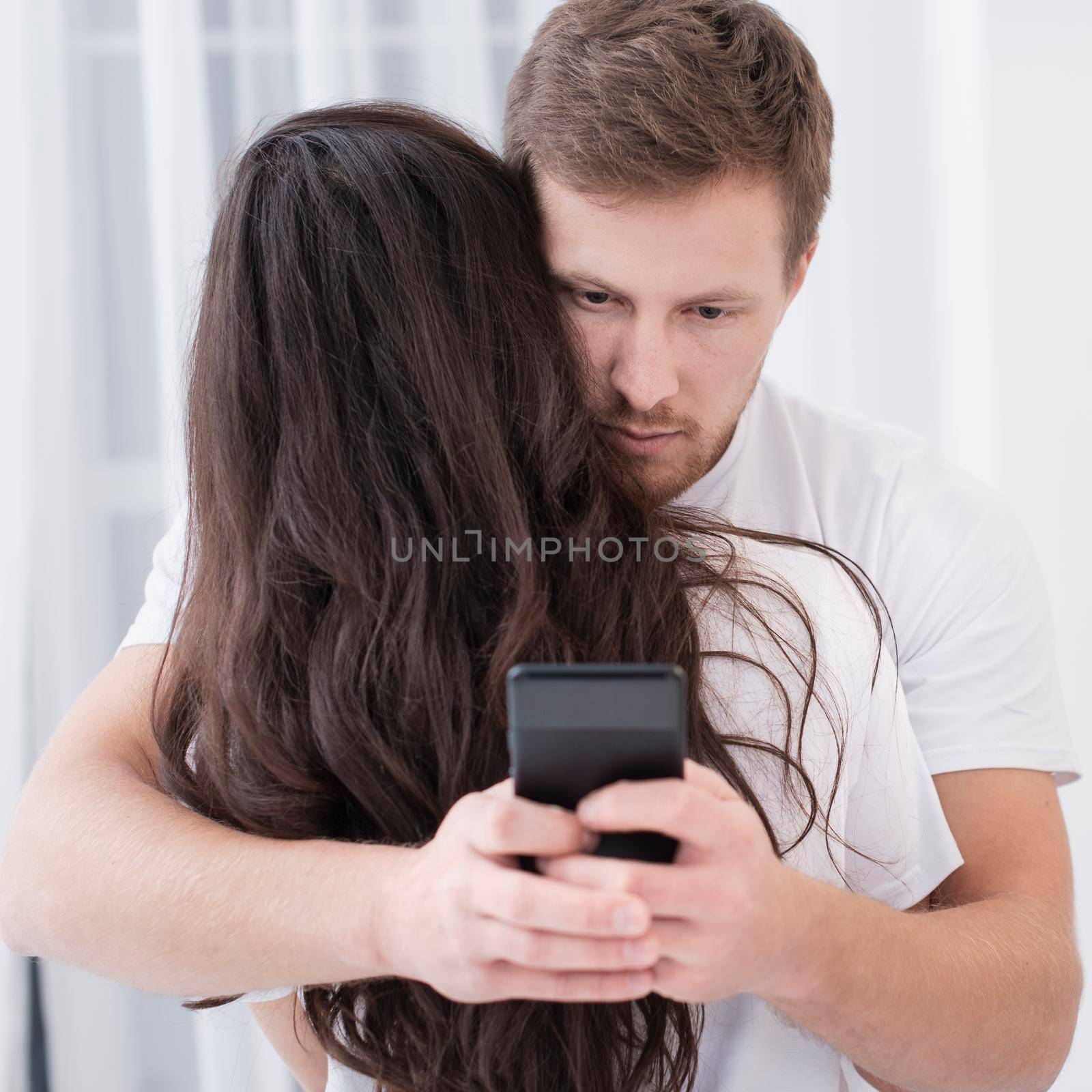 man hugging his girlfriend while checking his phone by Zahard