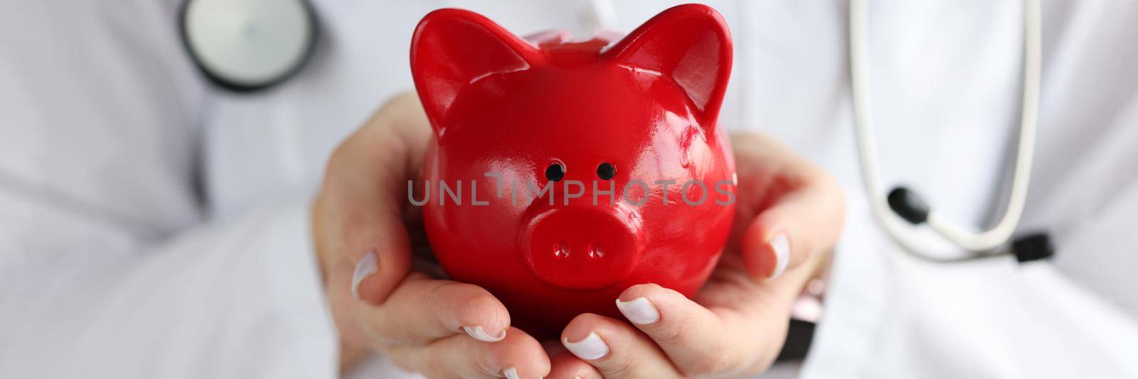 Doctor holding red piggy bank in his hands closeup by kuprevich