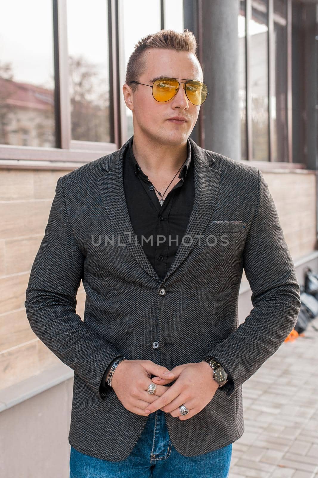 Stylish young guy portrait businessman of European appearance in a gray jacket and black shirt in sunglasses on the street outdoor by AYDO8