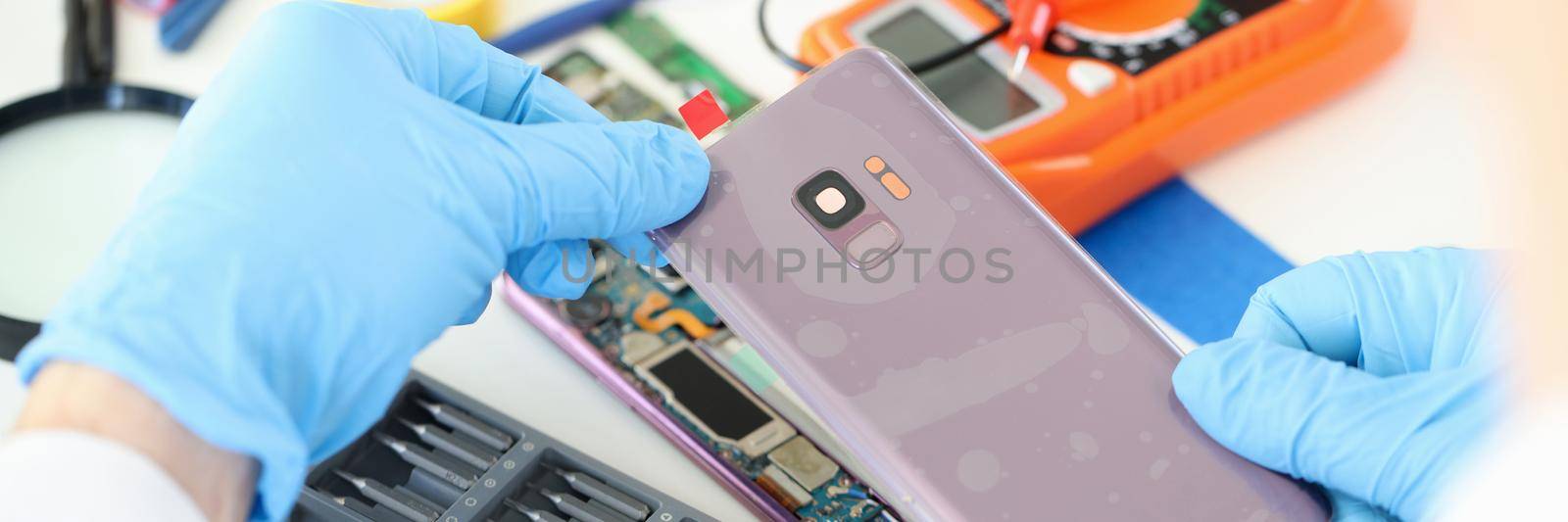 Craftsman in rubber gloves closing cover of mobile phone in workshop closeup. Mobile phone repair and service concept