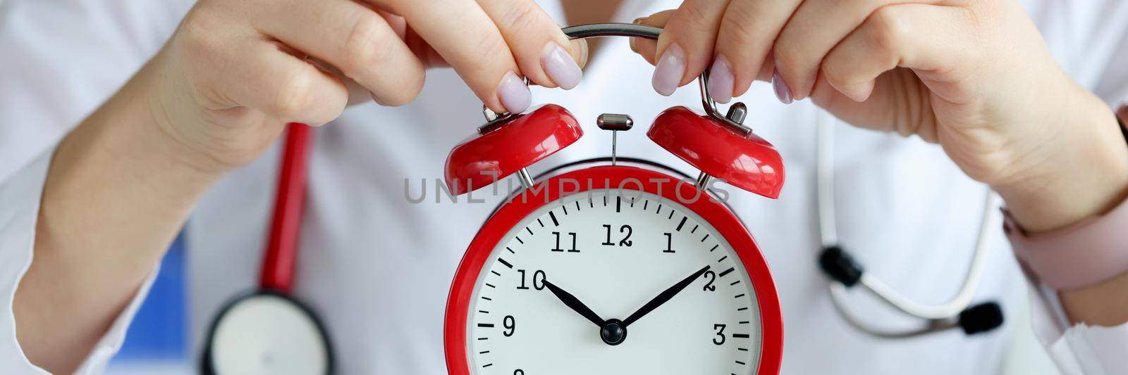 Doctor holding red alarm clock in clinic closeup. Regular intake of medications concept