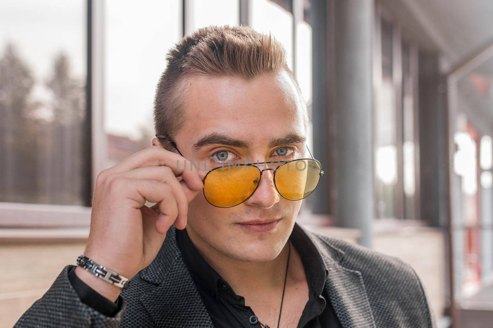 Portrait of a handsome man of European appearance businessman adjusting sunglasses with his hand, close-up on the outdoor of the street by AYDO8