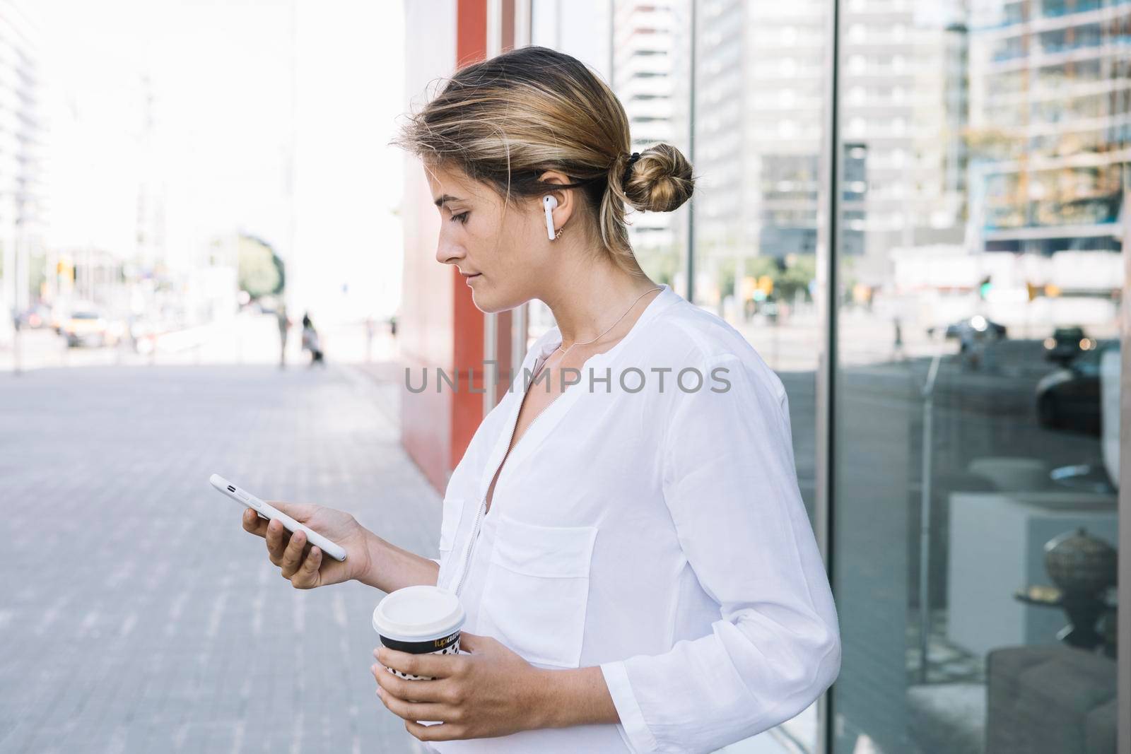 blonde young woman holding smart phone takeaway coffee cup hands