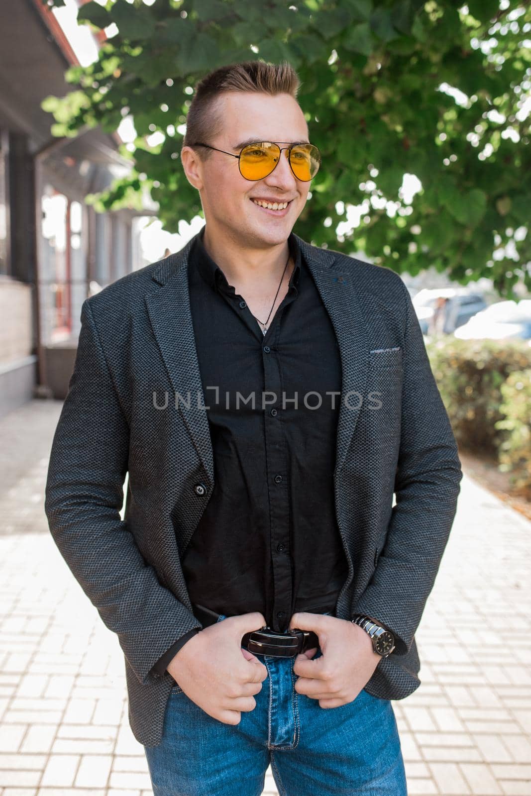 Stylish positive smiling young attractive guy of European appearance businessman portrait in jacket, shirt and jeans, in sunglasses on the street outdoor by AYDO8