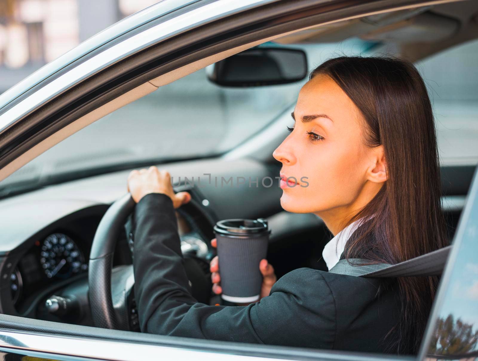 young businesswoman holding disposable coffee cup driving car by Zahard