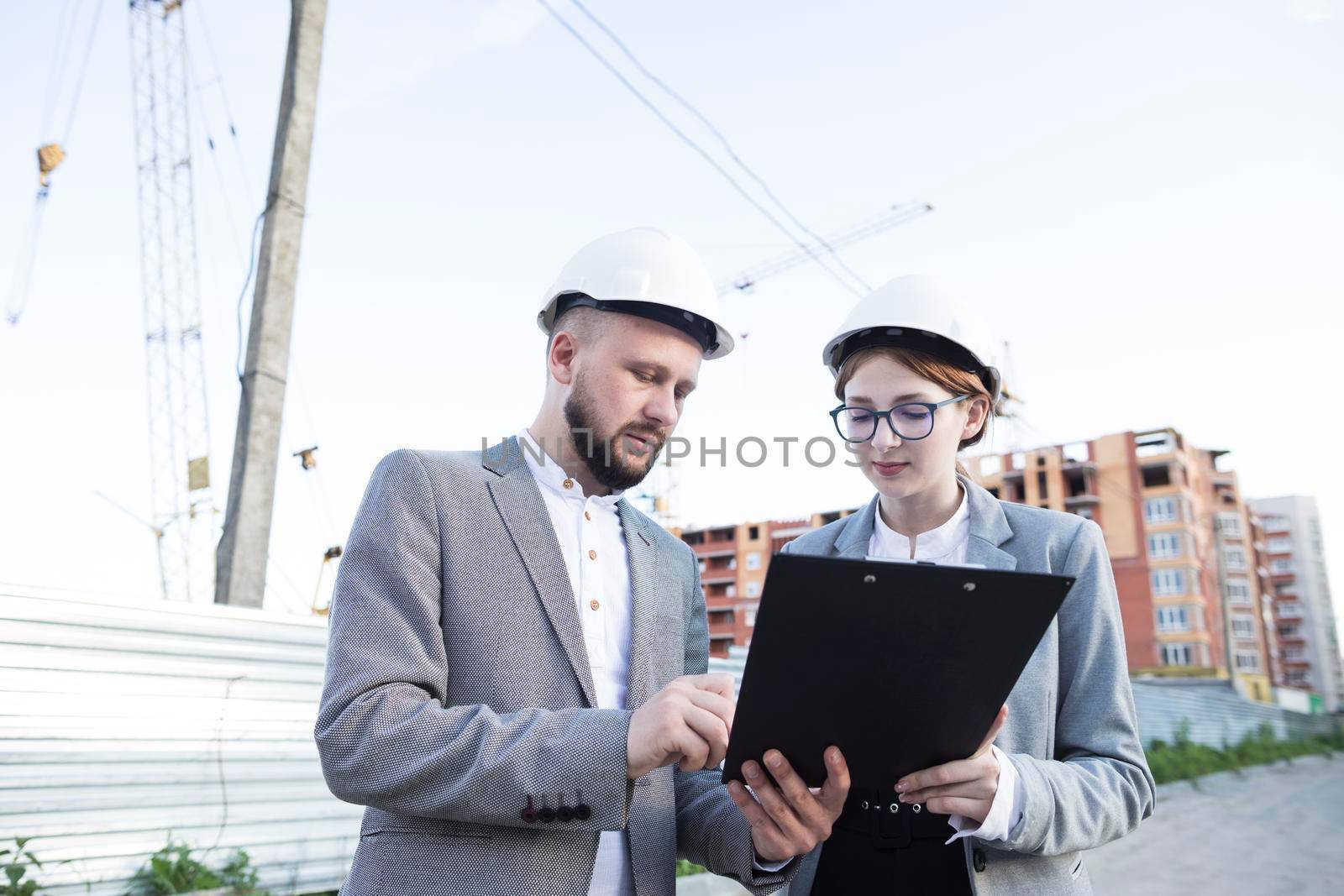 young female male architect wearing hard hat looking clipboard by Zahard