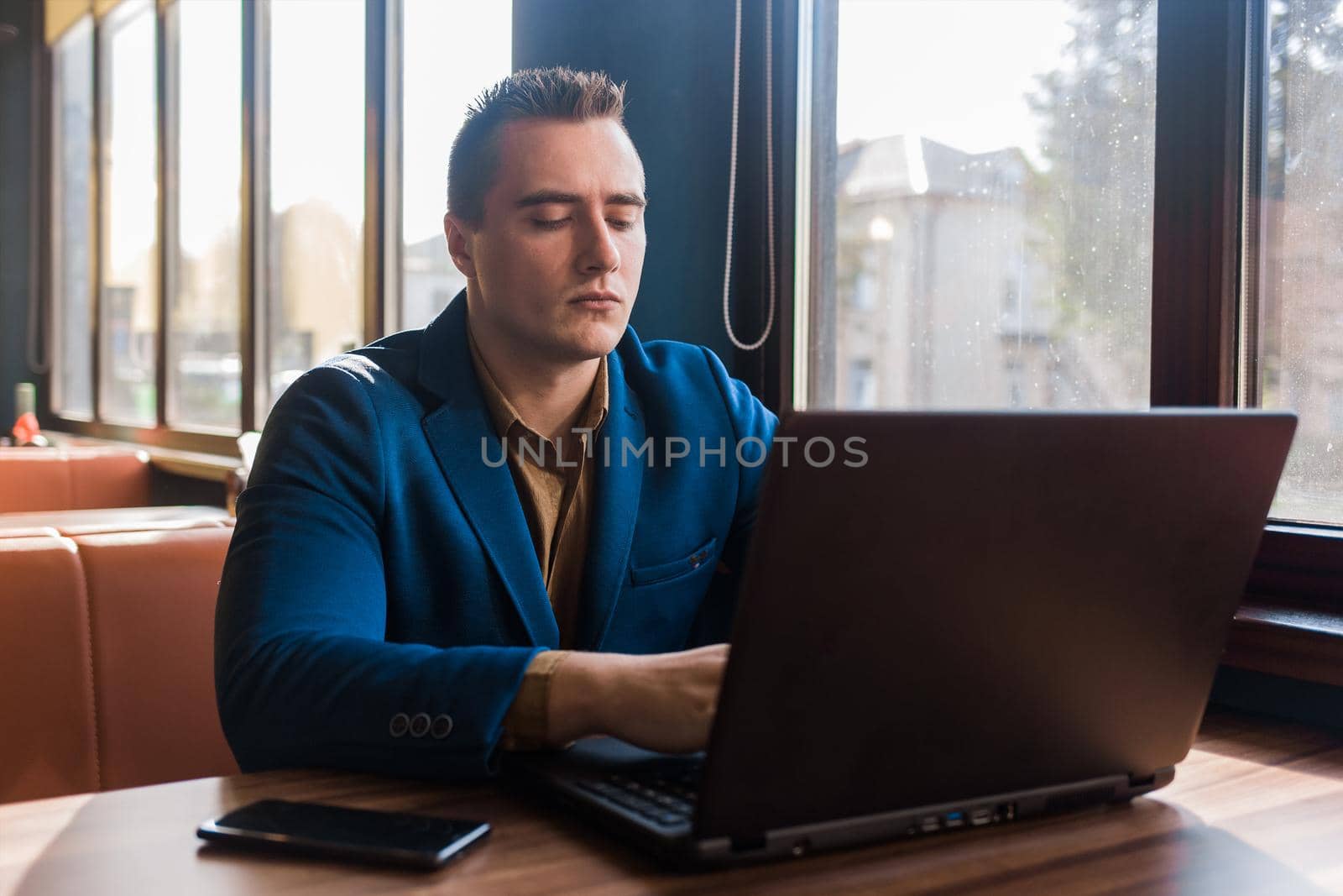 A business man businessman a stylish portrait of Caucasian appearance in a jacket and shirt, works in a laptop or computer, sitting at a table by the window in a cafe.