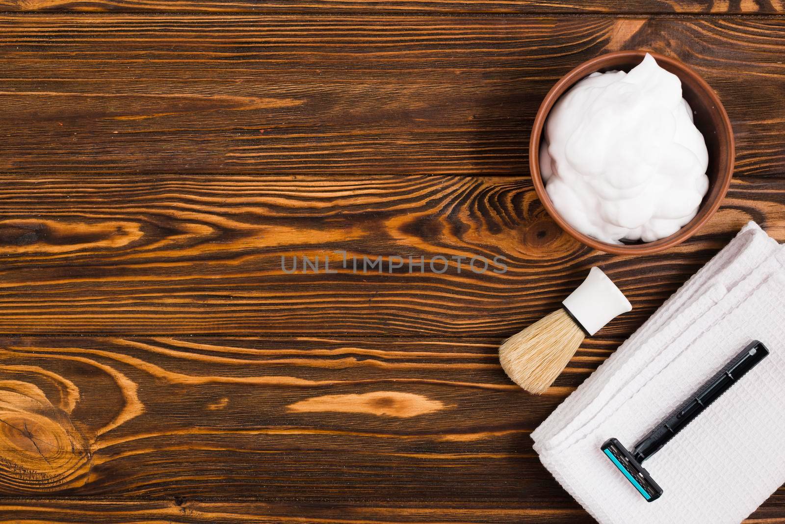 overhead view foam bowl shaving brush razor white folded napkin against wooden textured backdrop