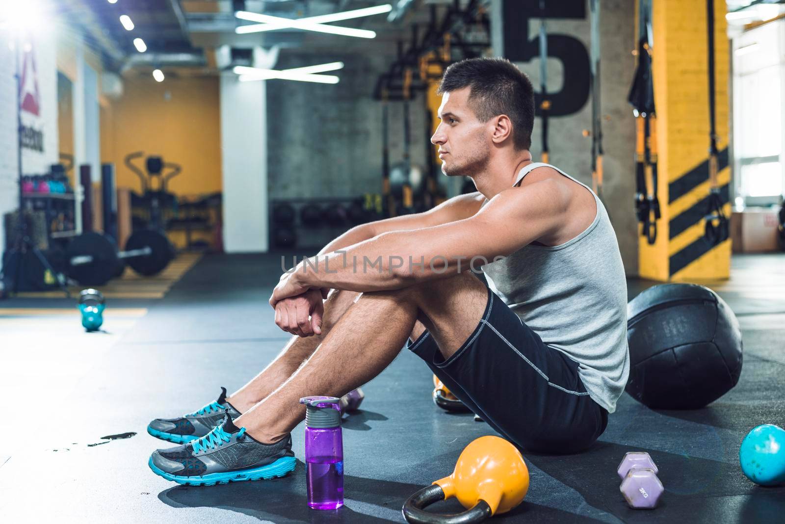 side view young man sitting floor near exercise equipments water bottle