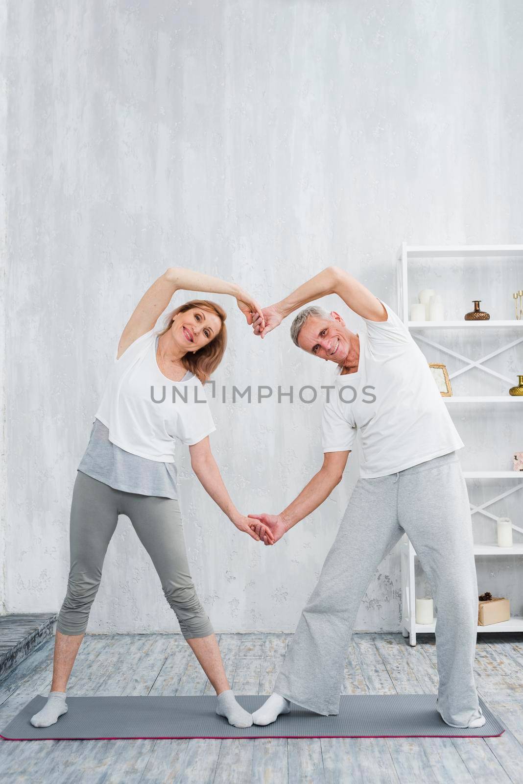 joyful senior couple making heart shape with their hands while exercising home by Zahard