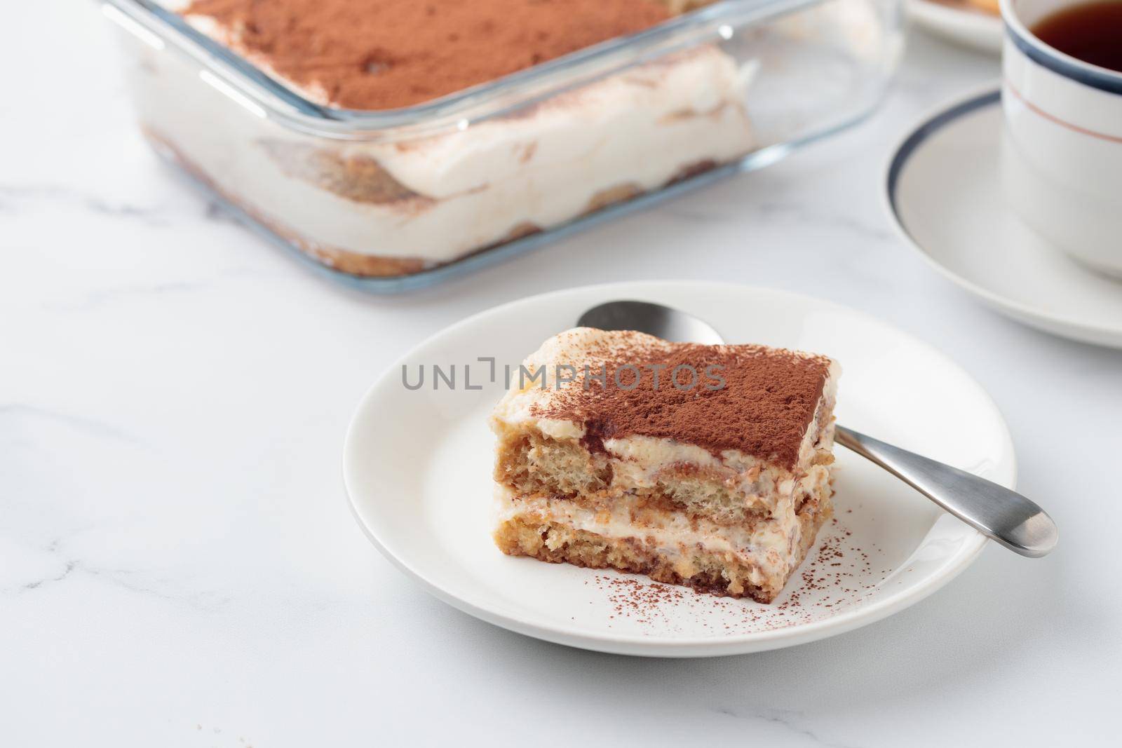 Piece of Homemade Tiramisu cake dessert on a white marble background