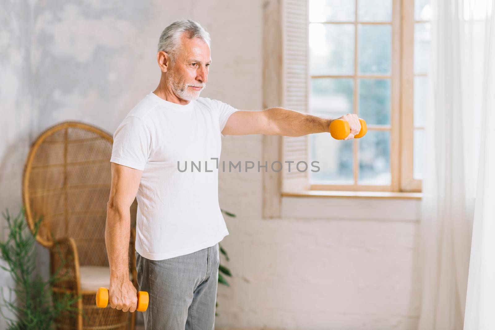 fit senior man exercising with orange dumbbells home by Zahard