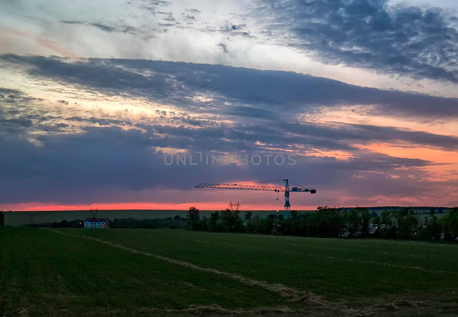Landscape with building and silhouette of the crane in the field.