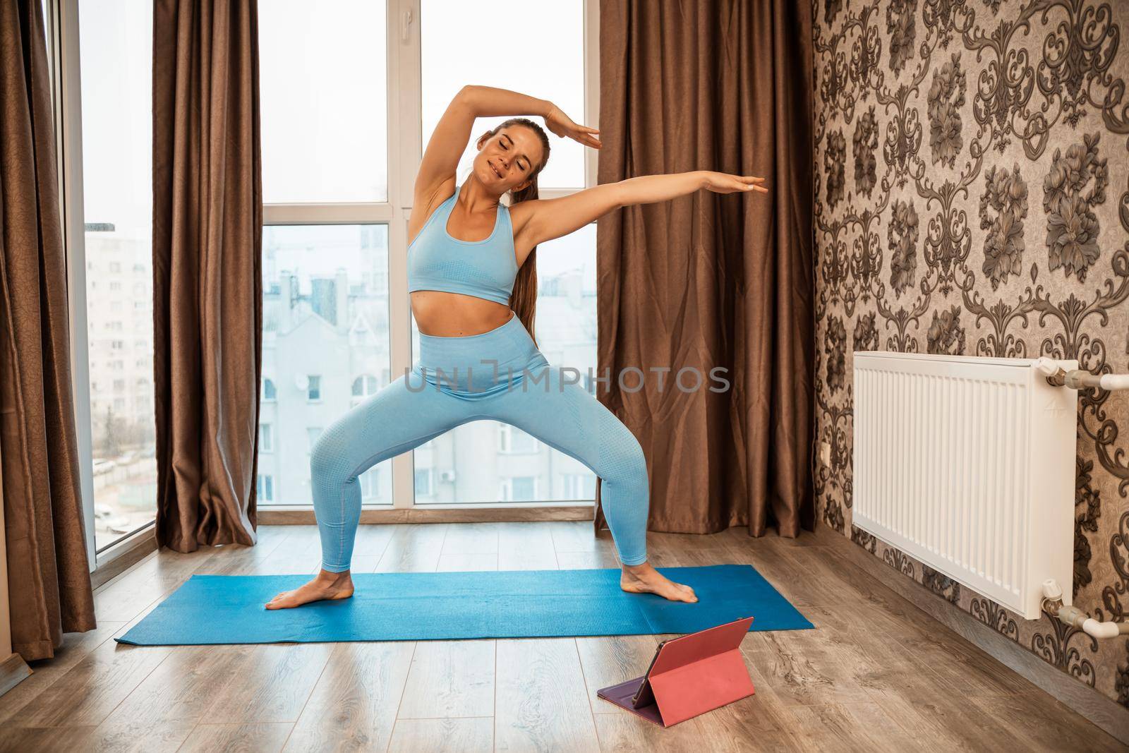 Young athletic attractive woman practicing yoga doing exercises. Works out at home or in a yoga studio, sportswear, blue pants and a full-length top indoors. Healthy lifestyle concept by Matiunina