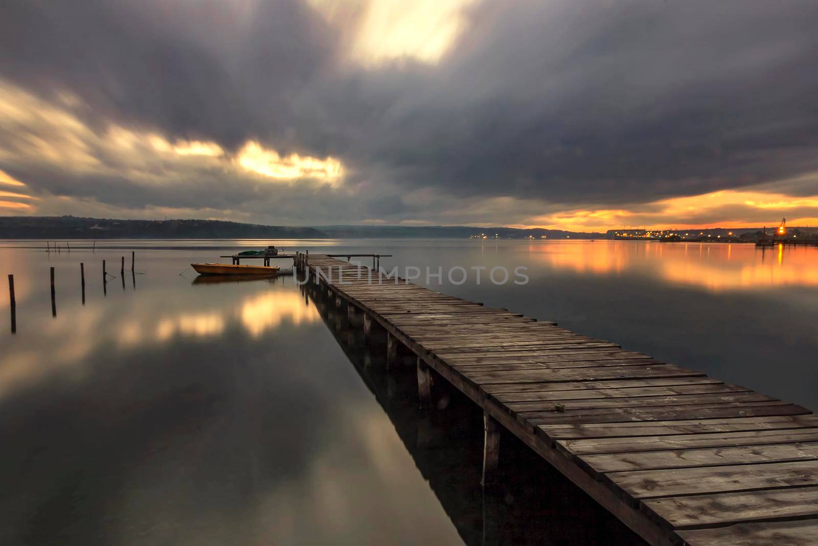 The long exposure view on a cloudy day on the lake with a boat at a wooden pier.