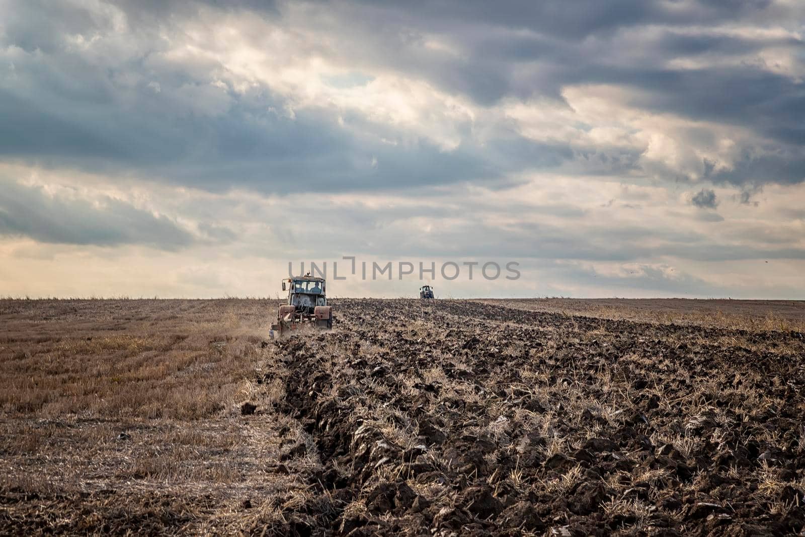 Day view of tractors plowing the soil in a mountain hill. Horizontal view