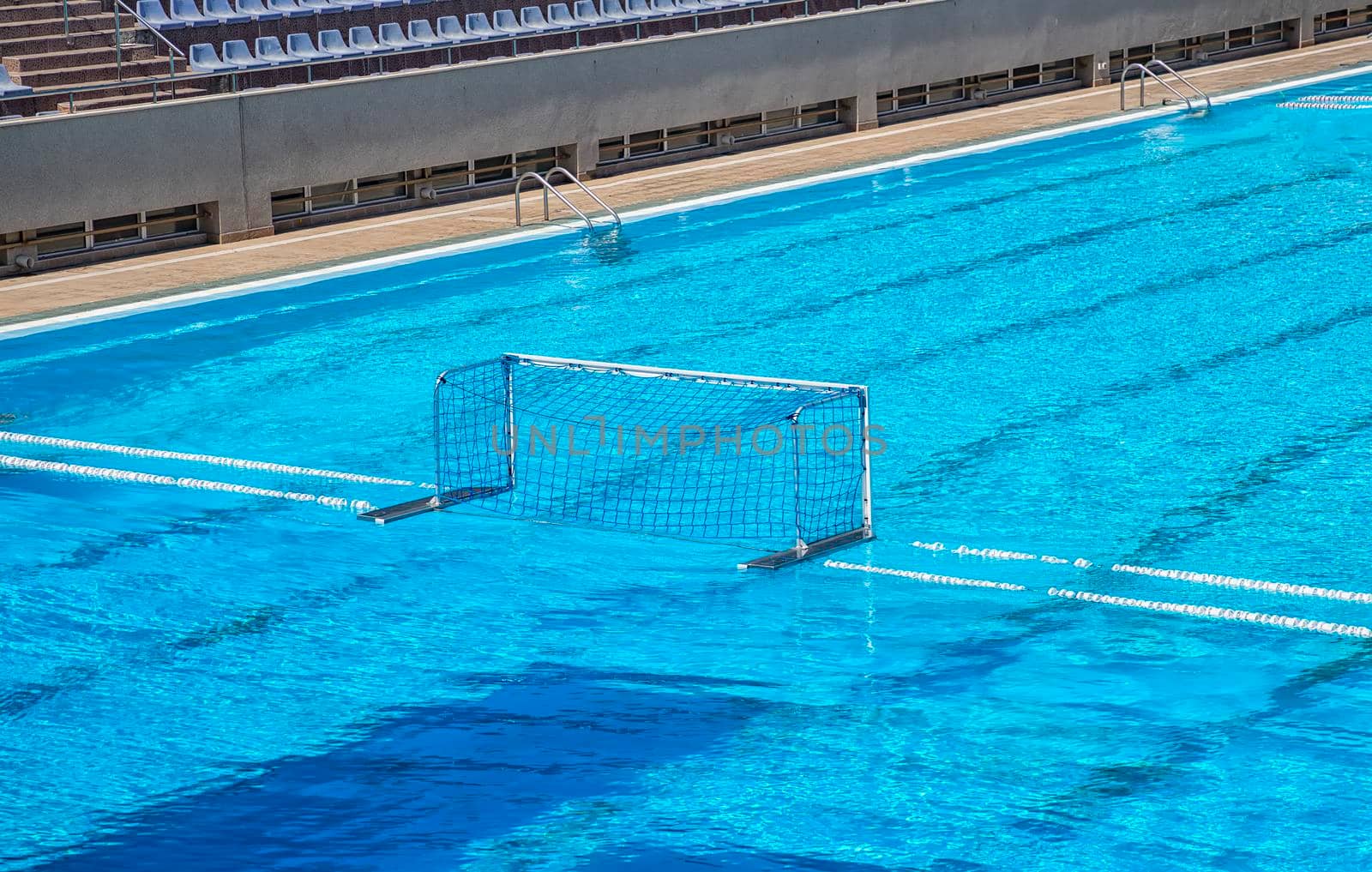 Empty water polo goal. Water sports equipment. Water polo goal with white frame and net supported with rope and floating buoys resting on the swimming pool.