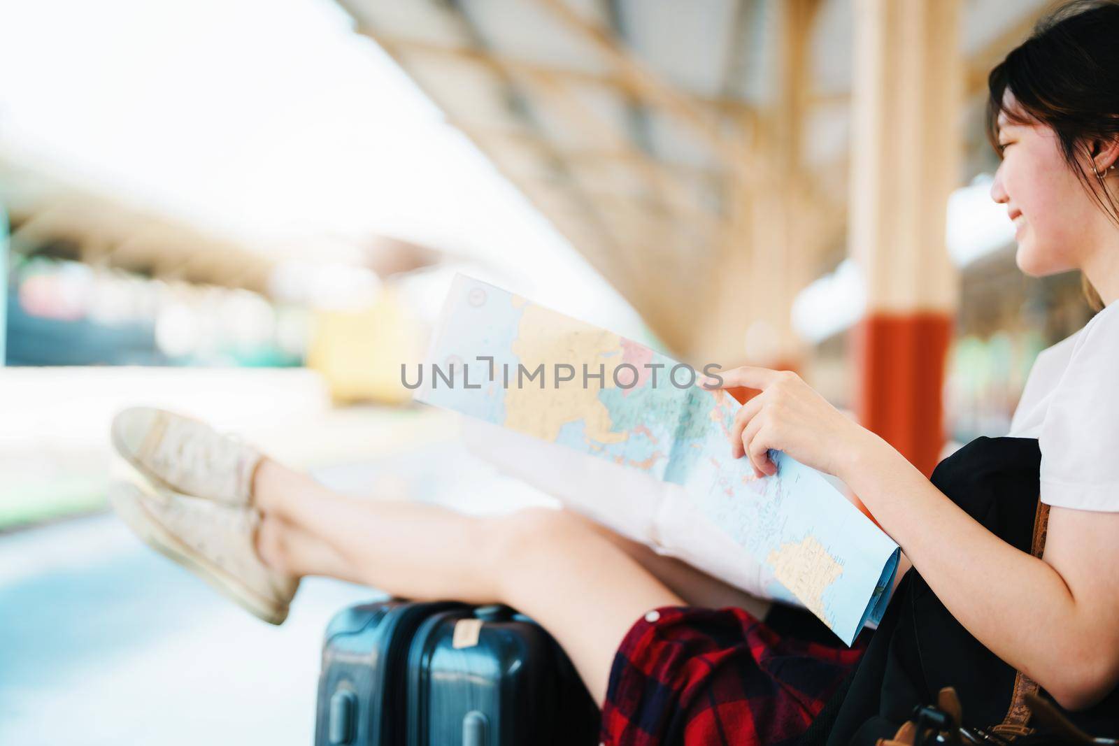 summer, relax, vacation, travel, portrait of a cute Asian girl looking at a map to plan a trip while waiting at the train station