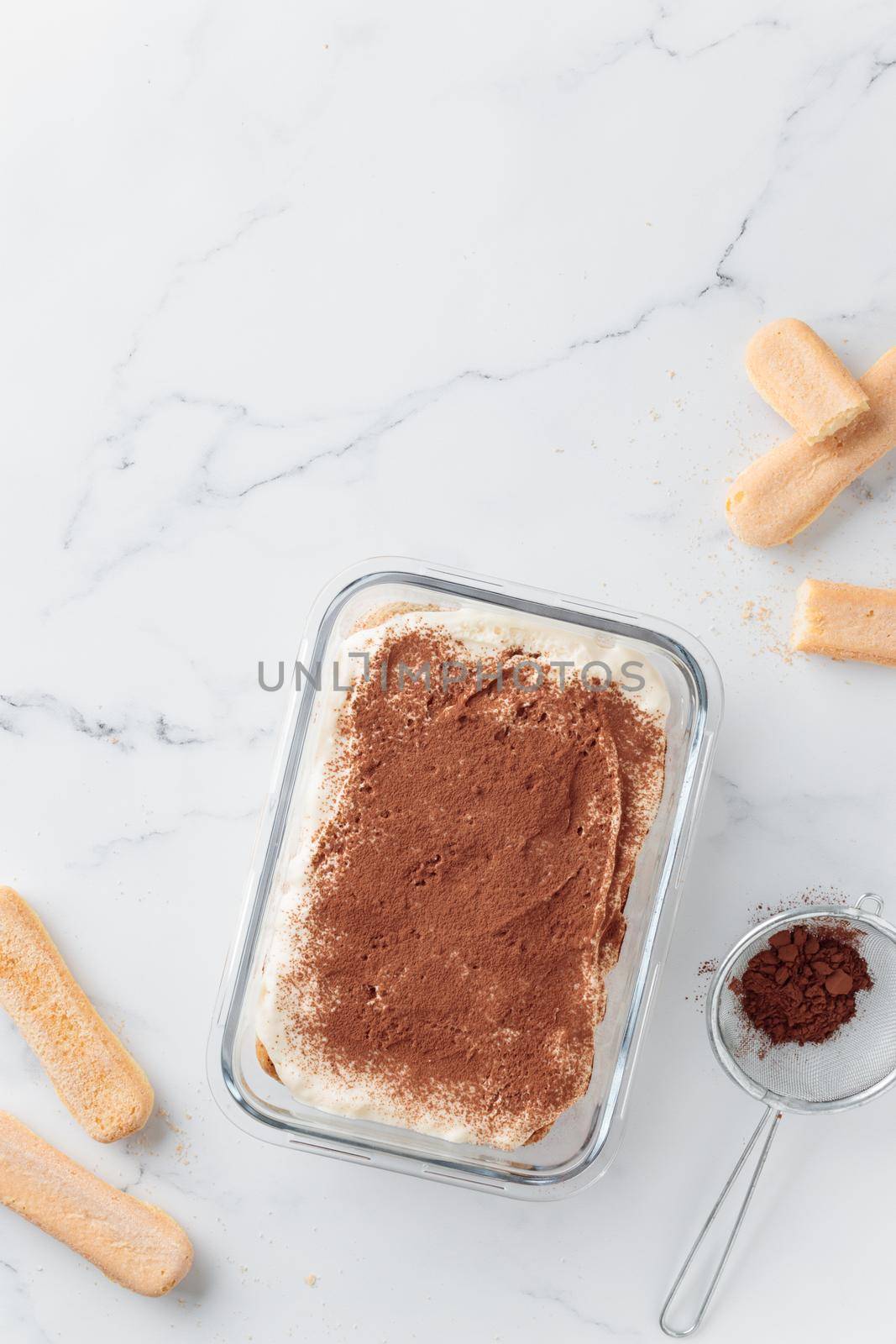 Homemade Tiramisu cake dessert and cocoa with savoiardi as ingredients on a white marble background