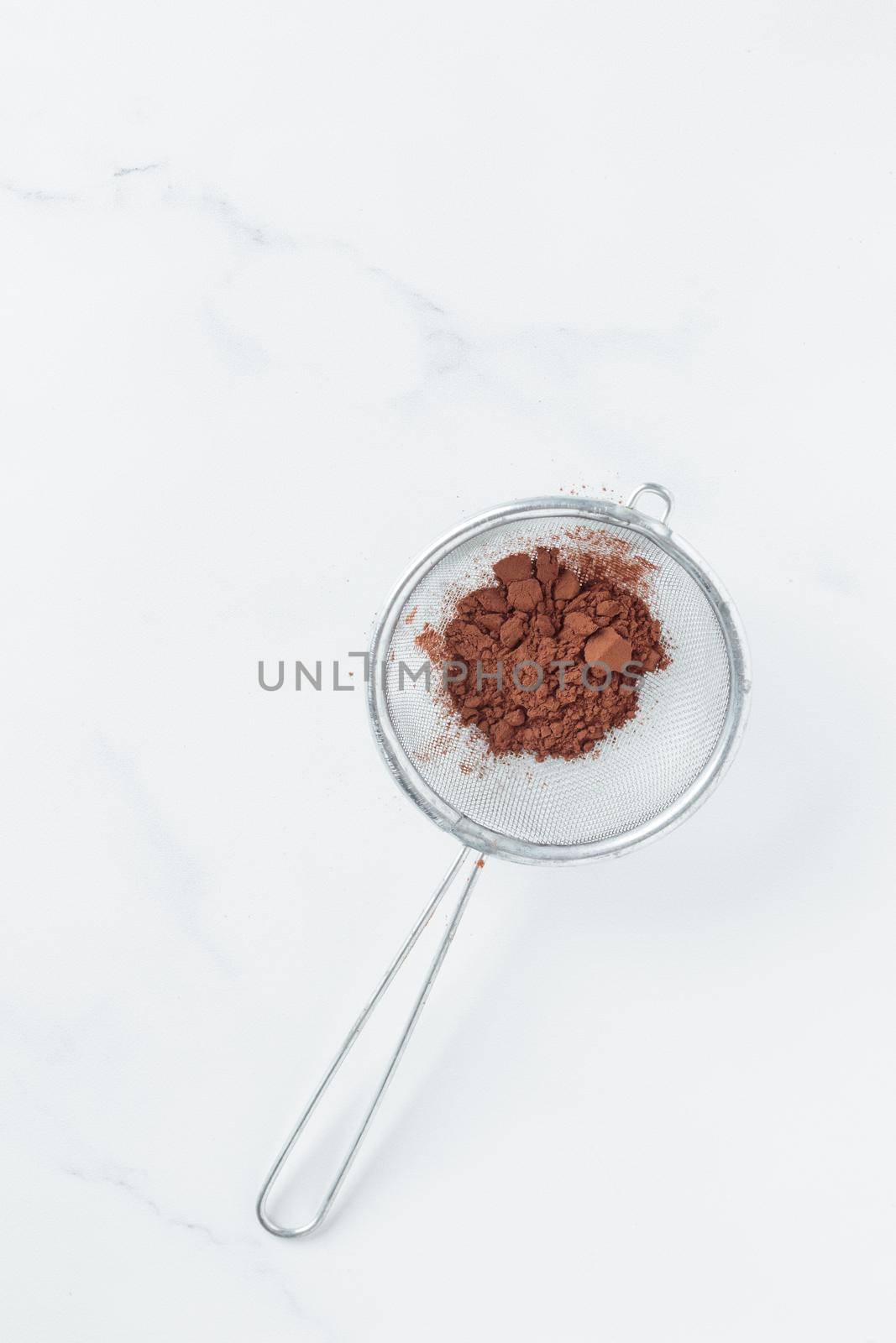Cocoa powder sweet ingredient in a strainer on a white backround top view