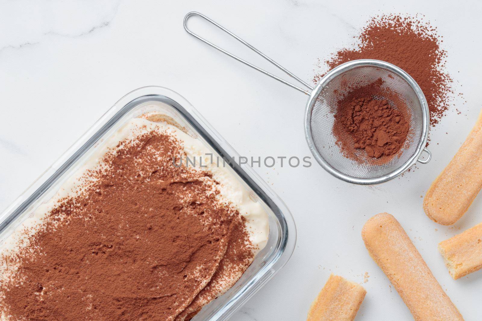 Homemade Tiramisu cake dessert and cocoa with savoiardi as ingredients on a white marble background