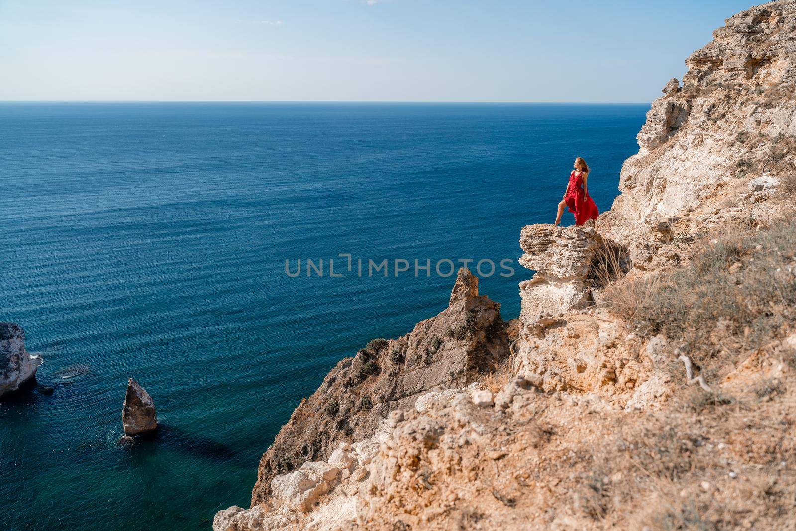 A woman in a red flying dress fluttering in the wind, against the backdrop of the sea