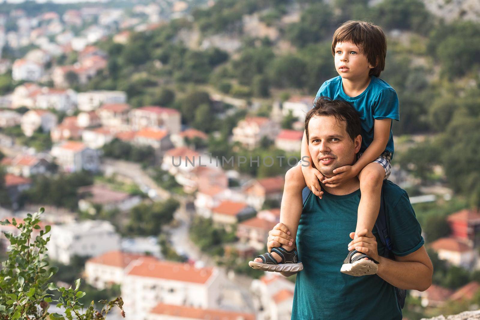 Father holding his little son on the sholders. Family hiking in the mountains with the panoramic view of the old Mediterranean city behind them. Kotor Bay in Montenegro