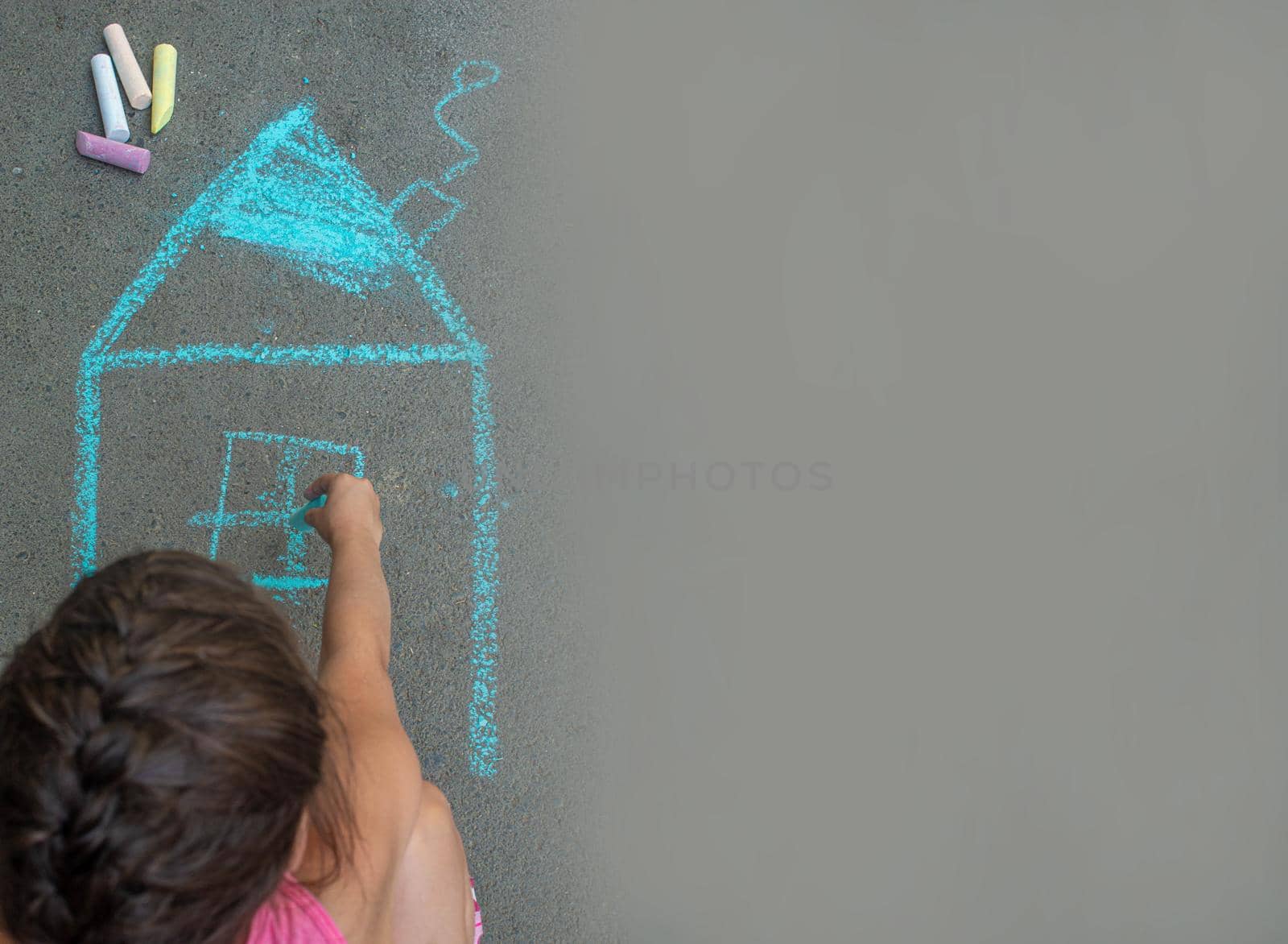The child draws the house with chalk on the asphalt. Selective focus. by mila1784