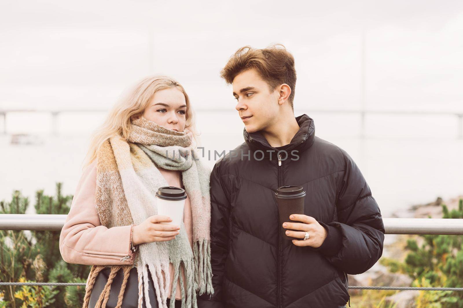 Lovely brunette guy and pretty girl blonde drink coffee and talking on a date. Loving teenagers are happy, smiling, laughing. Teen Love Concept. Outdoor.