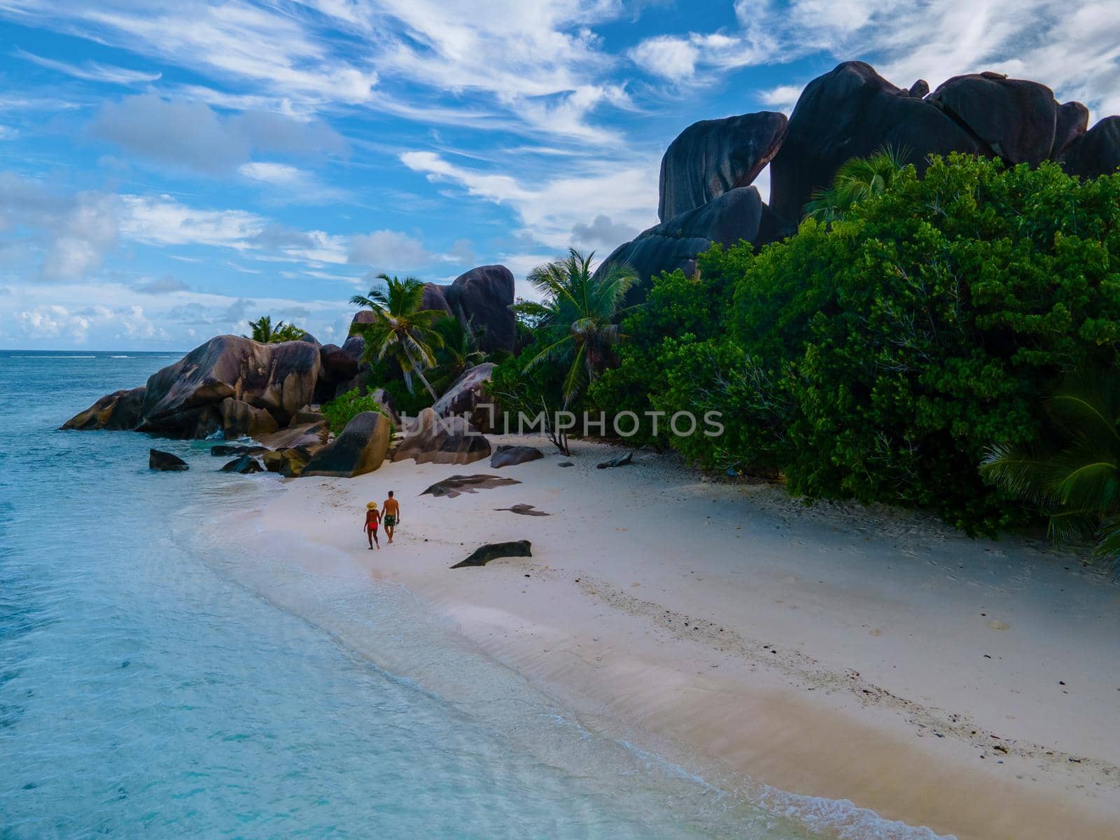 Anse Source d'Argent beach, La Digue Island, Seyshelles, Drone aerial view of La Digue Seychelles bird eye view, couple men and woman walking at the beach during sunset at a luxury vacation by fokkebok